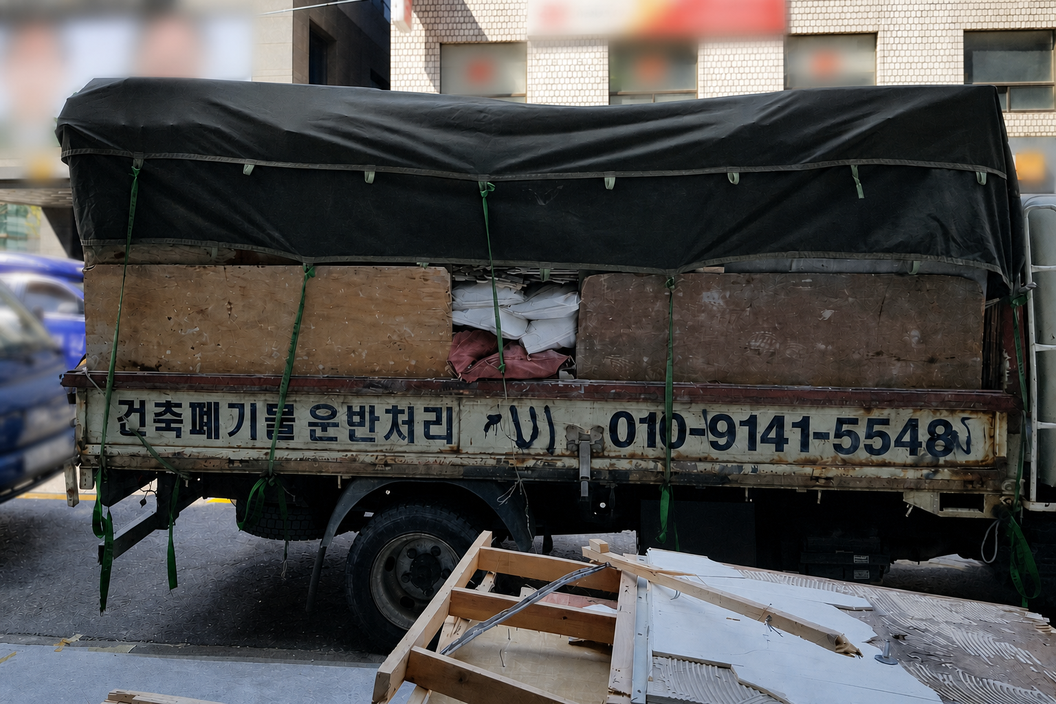 합판 측판과 검은색 방수덮개를 고정한 2.5톤 철거폐기물 운반 차량